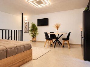 A modern bedroom with a bed, a dining table with chairs, a potted plant, and a TV on the wall.