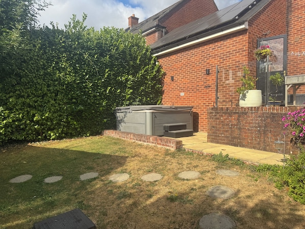 A brick house with a large hedge, a patio with stepping stones, and a grey outdoor heater.