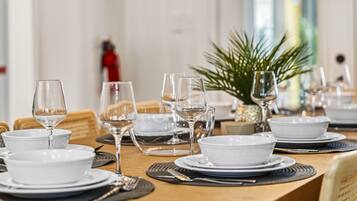 Una mesa de comedor dispuesta con platos, cuencos y copas de vino, con una planta al fondo.