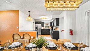 Un'area pranzo con tavolo apparecchiato per sei, una cucina sullo sfondo e un estintore fissato al muro.