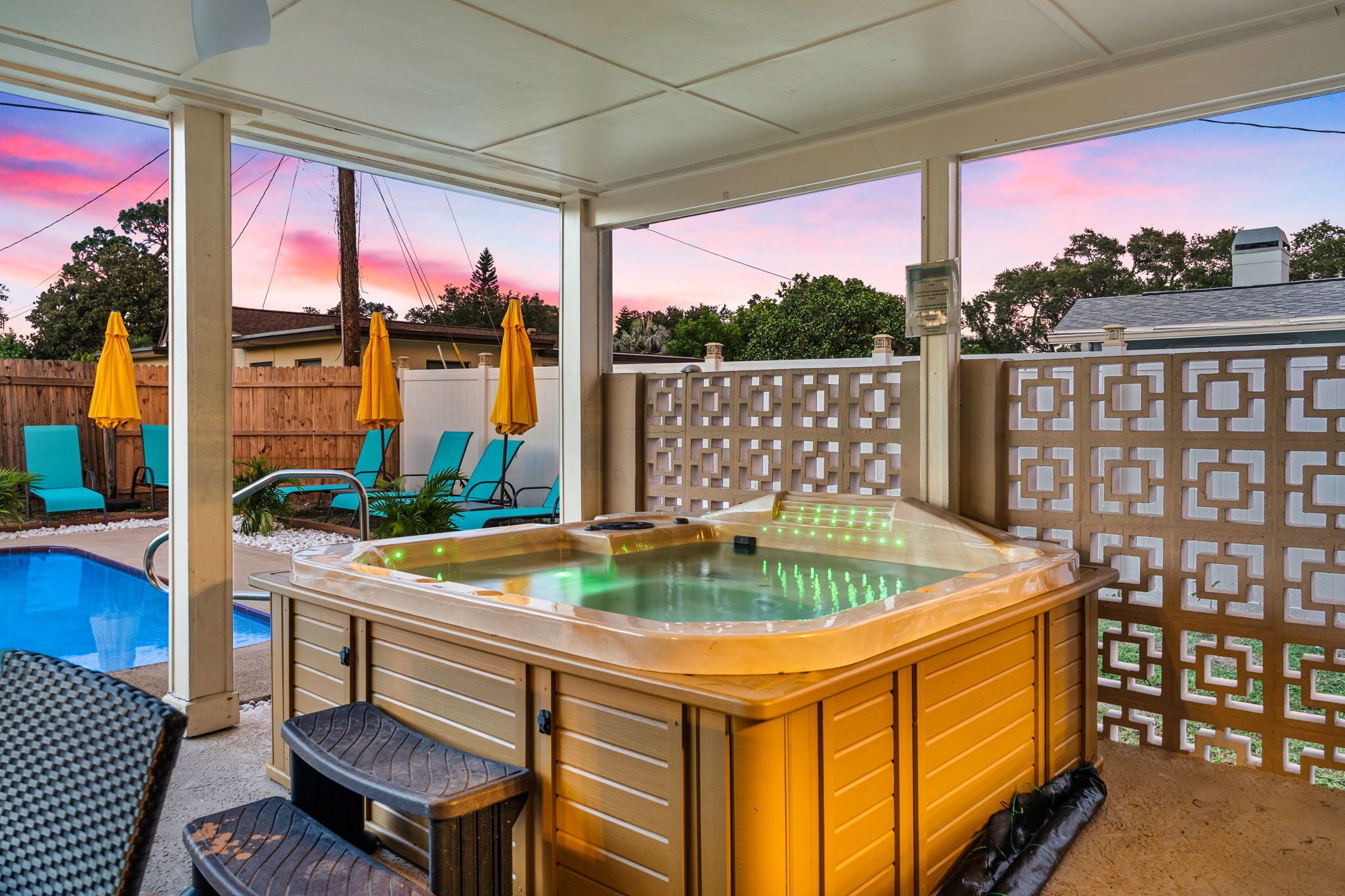 A hot tub with a wooden exterior, a pool, and outdoor seating with umbrellas.
