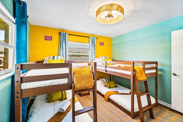 A room with bunk beds, a ceiling fan, and a window with curtains.