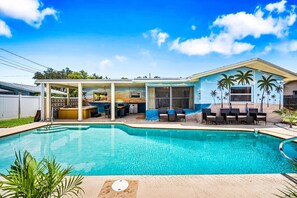 A swimming pool with a covered patio area, outdoor seating, and a mural of a beach scene.