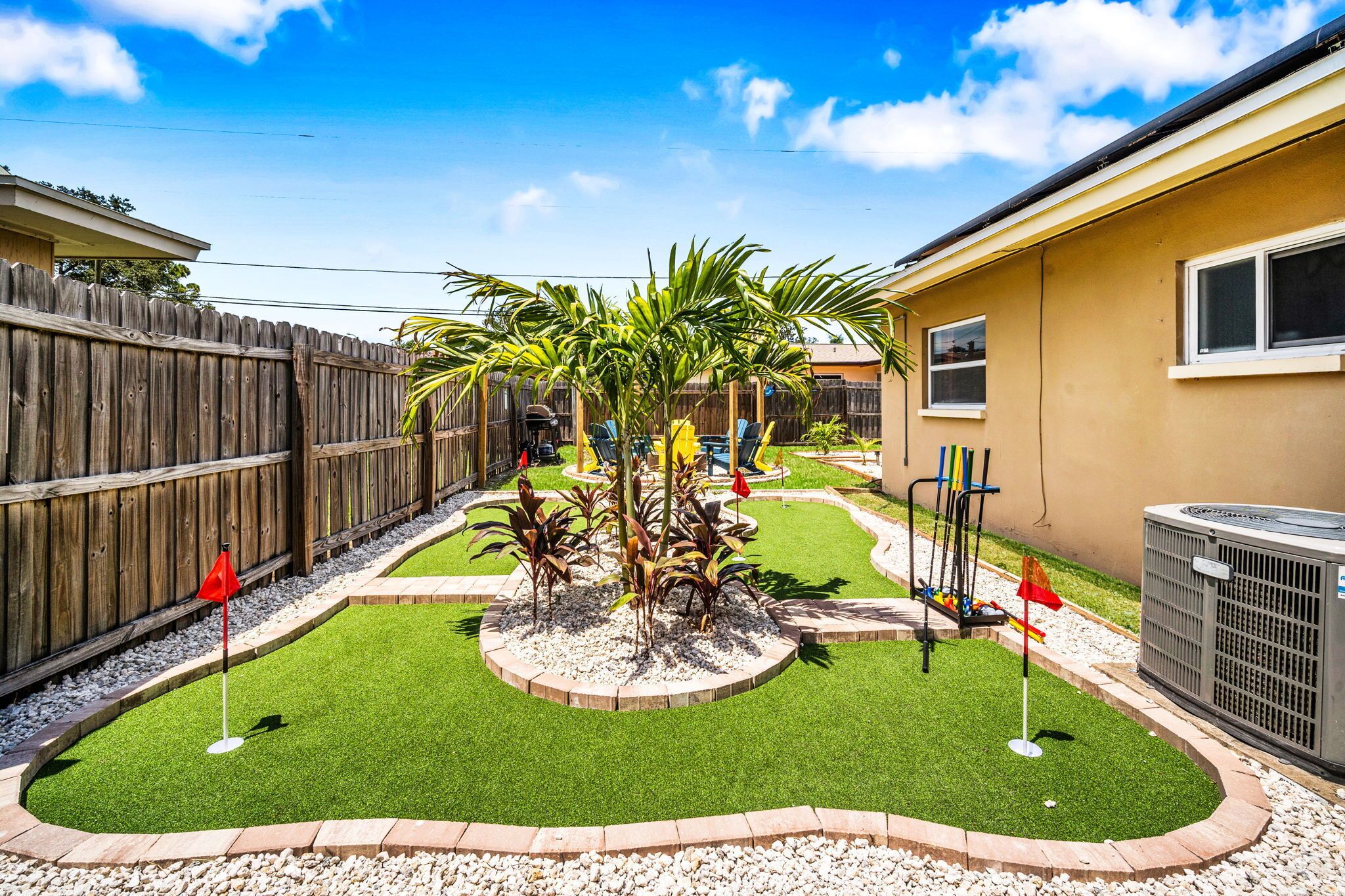 A backyard with artificial grass, a palm tree, and a wooden fence.