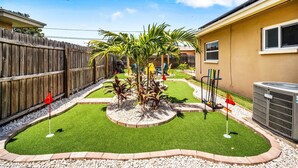 Un giardino sul retro con erba sintetica, una palma e un recinto in legno.