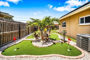 A backyard with artificial grass, a palm tree, and a wooden fence.