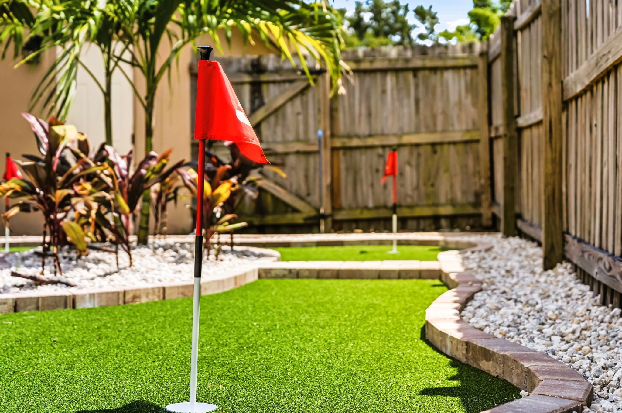 Un campo de mini golf con césped artificial, banderas rojas y una valla de madera al fondo.