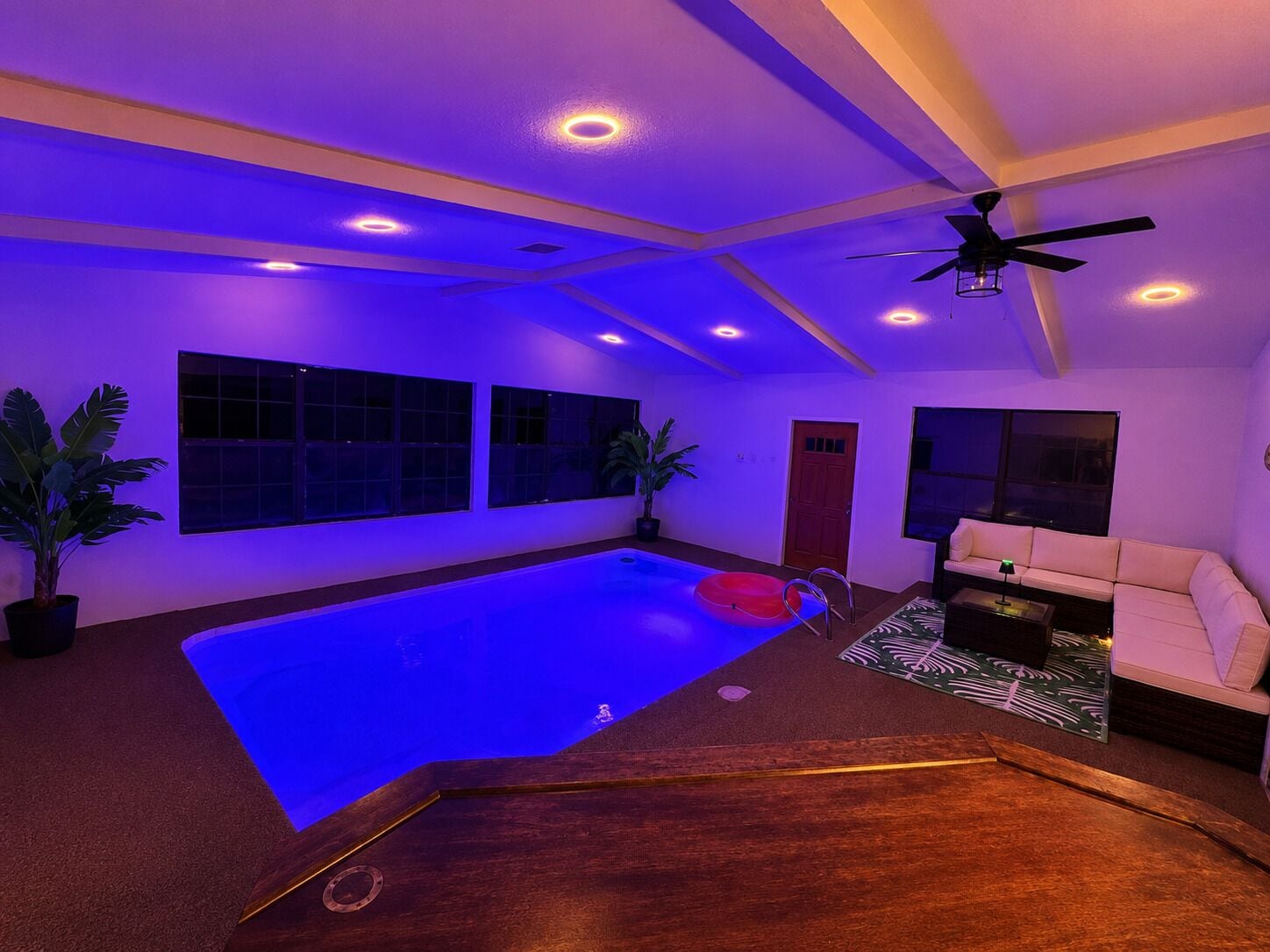 A room with a blue-lit pool, a ceiling fan, and a sofa.