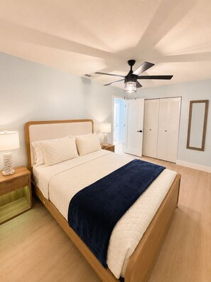 Ein Schlafzimmer mit Bett, Nachttisch, Lampe, Deckenventilator, Kleiderschrank und Spiegel.