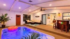 Ein Poolbereich mit Whirlpool, einer Sitzgruppe inklusive Sofa und Sesseln sowie eine Bar mit Hockern.