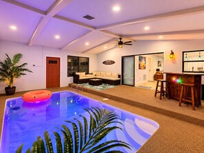 A pool area with a hot tub, a seating area with a sofa and chairs, and a bar with stools. - The Tiki Hideaway - Indoor Pool. Tiki Bar. Modern Beach Vibes (Homosassa)