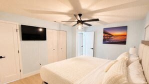 Ein Schlafzimmer mit einem Bett, einem Deckenventilator, einem an der Wand montierten Fernseher und einem Gemälde.