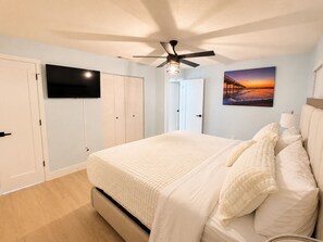 A bedroom with a bed, a ceiling fan, a TV mounted on the wall, and a painting. - The Tiki Hideaway - Indoor Pool. Tiki Bar. Modern Beach Vibes (Homosassa)