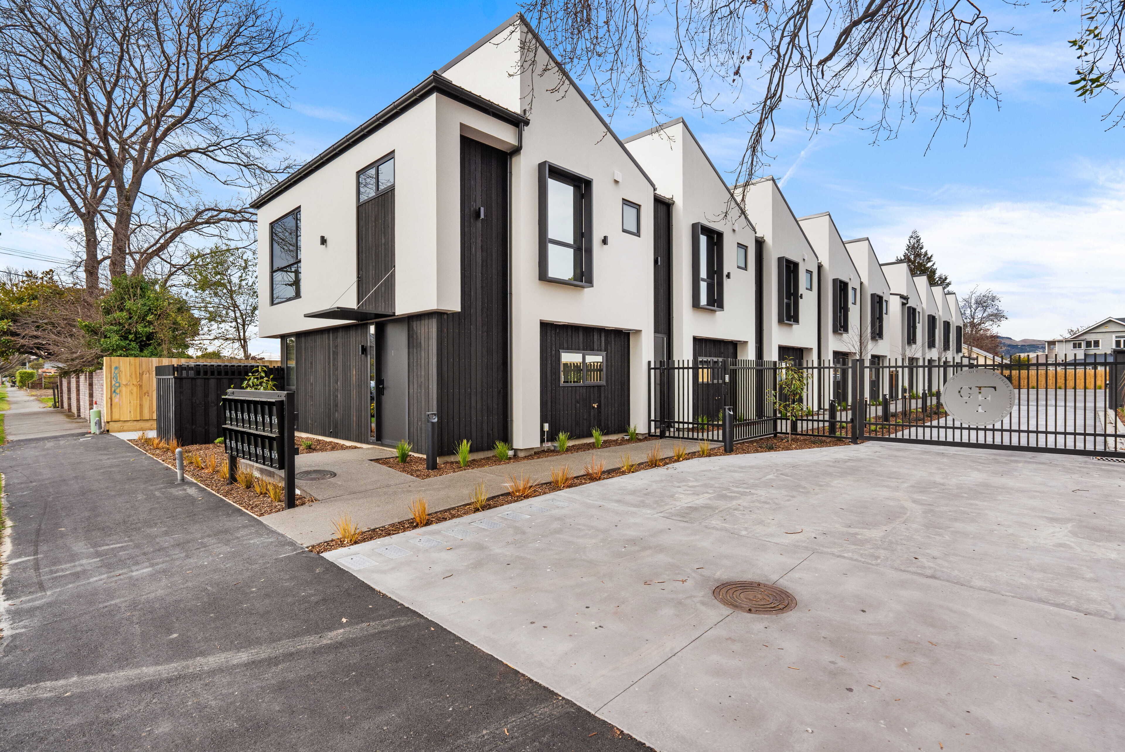 Um edifício residencial moderno com telhado plano, janelas amplas e entrada com portão.