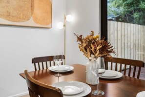 A dining table with chairs, a vase with dried flowers, and wine glasses. - Secure Quiet CBD Christchurch Townhouse | Free Parking + EV (Christchurch)