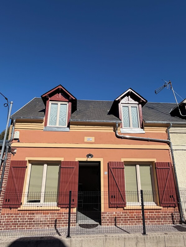 A two-story building with a red and beige facade, a visible door, and a small sign above the entrance. - Amel's House by the Sea (Ault)