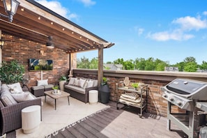 An outdoor patio with a brick wall, a sofa set, a grill, and a view of the sky. - The Bentonville Brownstone | Luxury Stay Downtown (Bentonville)