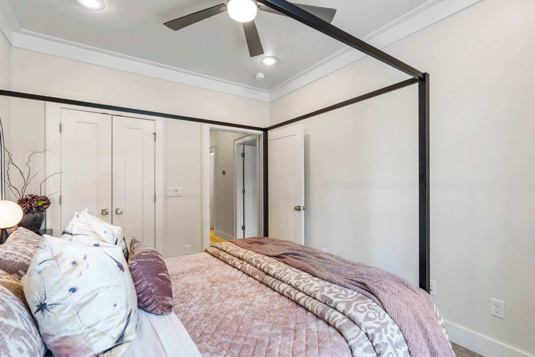 A bedroom with a bed, a ceiling fan, and a door leading to another room.