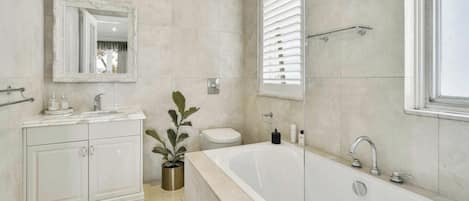 A bathroom with a bathtub, toilet, vanity with cabinets, a mirror, and a potted plant.