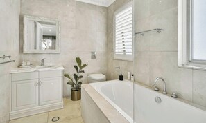 A bathroom with a bathtub, toilet, vanity with cabinets, a mirror, and a potted plant. - Villa Sydney (Hunters Hill)