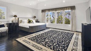 Een slaapkamer met een groot bed, een nachtkastje, een stoel, een bureau en uitzicht op bomen door het raam.