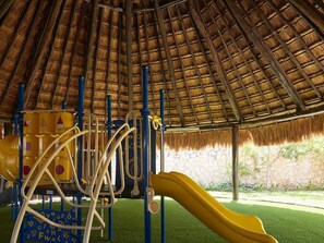 Ein Spielplatz mit einem Reetdach, einer gelben Rutsche und Klettergerüsten.