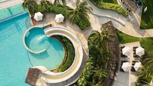 Una piscina circolare con una passeggiata circostante, palme e zone relax all'aperto.