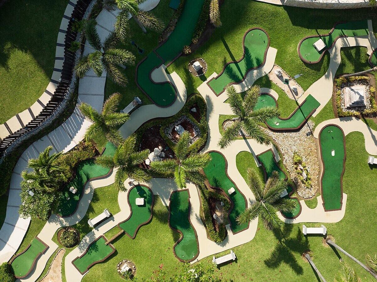A golf course with multiple green areas, pathways, and palm trees.