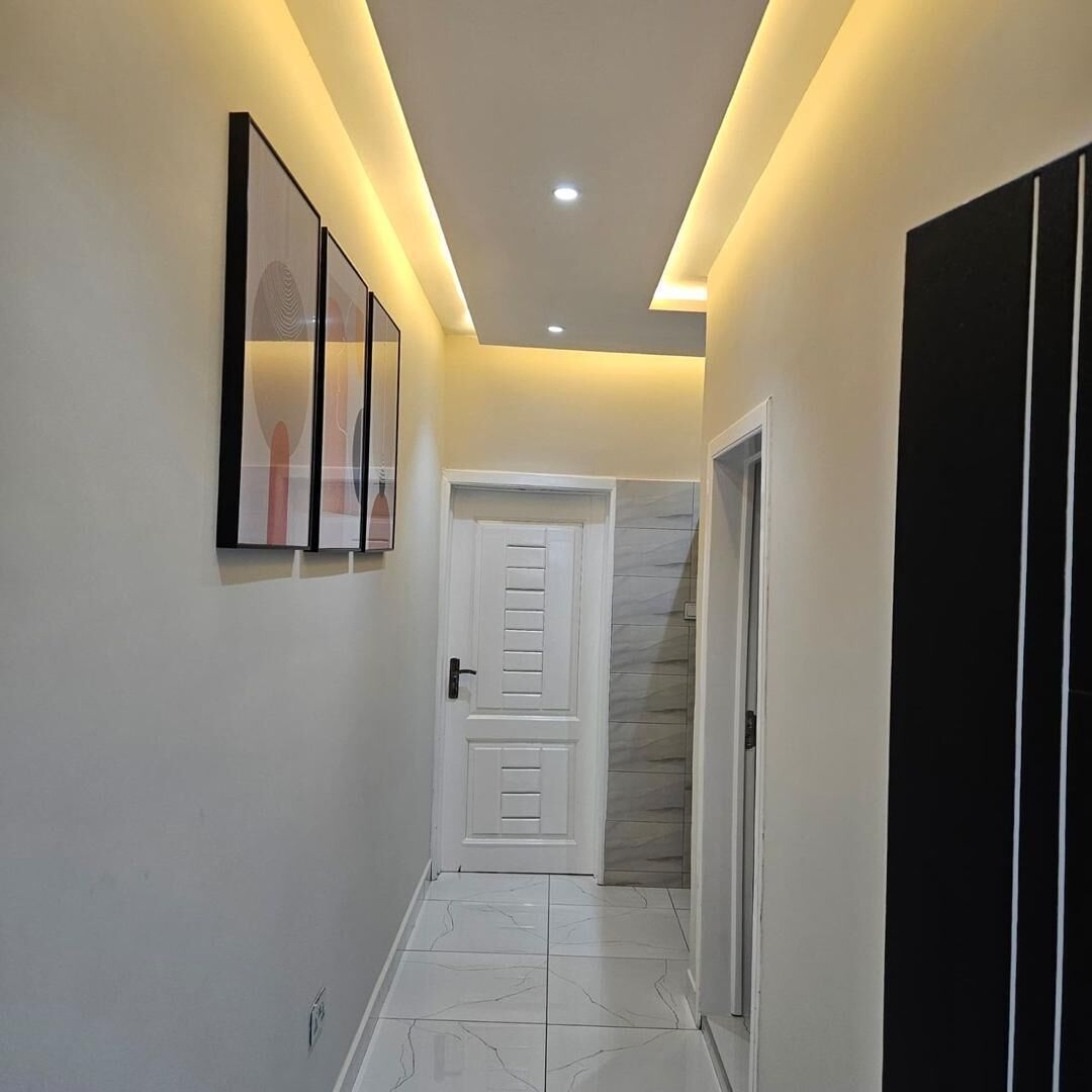 Un couloir avec une porte blanche, une armoire noire et une œuvre d’art encadrée accrochée au mur.