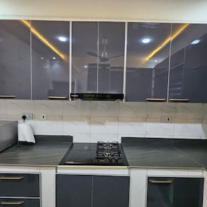 A kitchen with a black stove, white cabinets, and a ceiling fan. - Cozy 1-Bedroom Apartment in Dansoman Control, Enjoy comfort, style and beauty. (Accra)