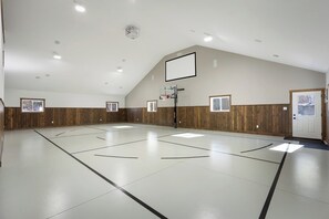 An indoor basketball court with a wooden wall paneling, a basketball hoop, and a door with a window. - Courtside Cabin
Gym- Hot Tub- Events (Nisswa MN)