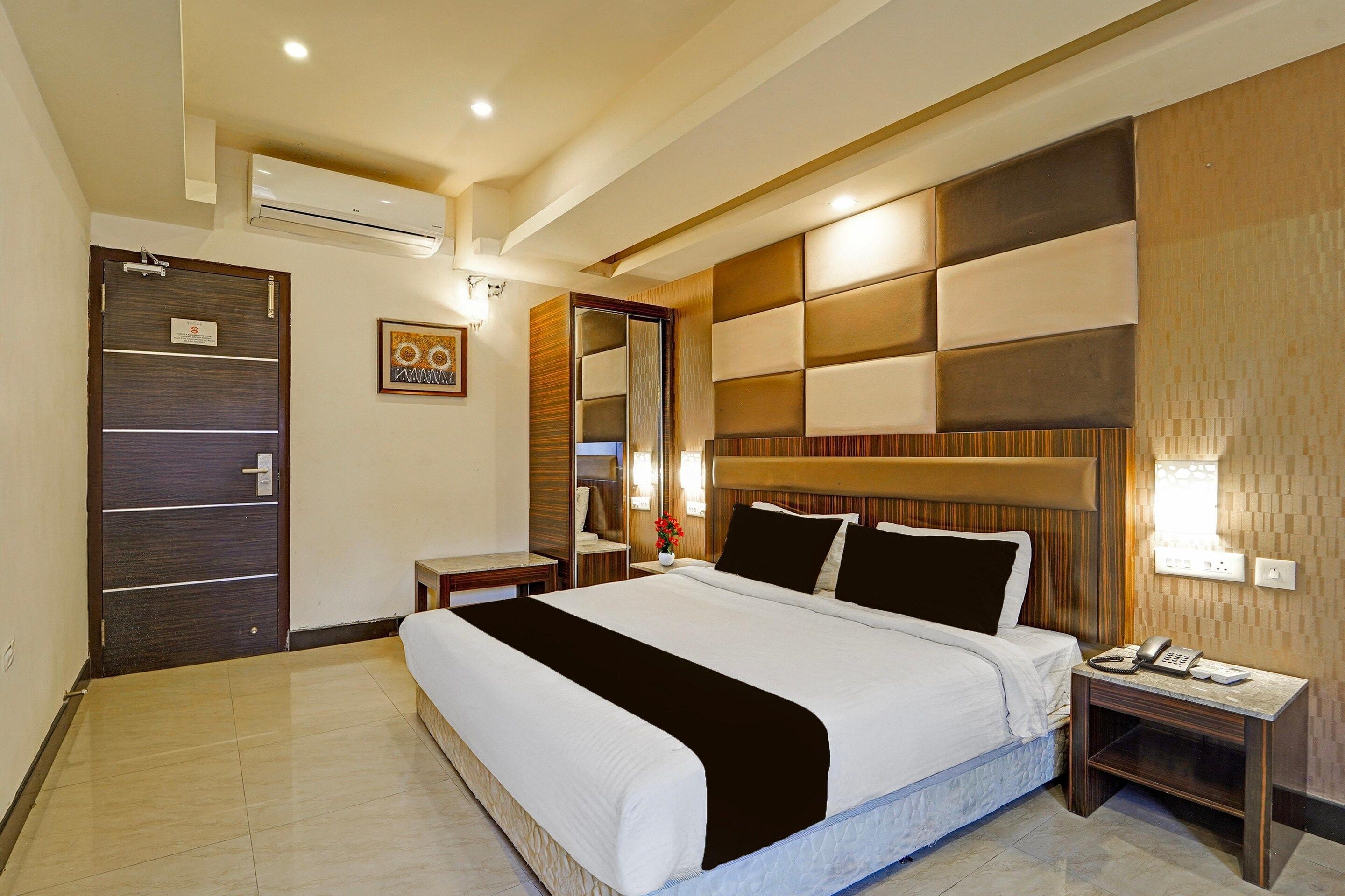 Quarto de hotel com uma cama grande, mesa de cabeceira, espelho e porta com uma placa.