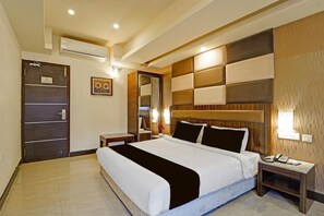 A hotel room with a large bed, a bedside table, a nightstand, a mirror, and a door with a sign. - Deluxe Room RK Residency (Coimbatore)