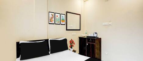 A hotel room with a large bed, a small table with a kettle, and a cabinet.