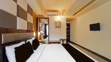 A hotel room with a large bed, a bedside table, a mirror, a small table, and a TV mounted on the wall.