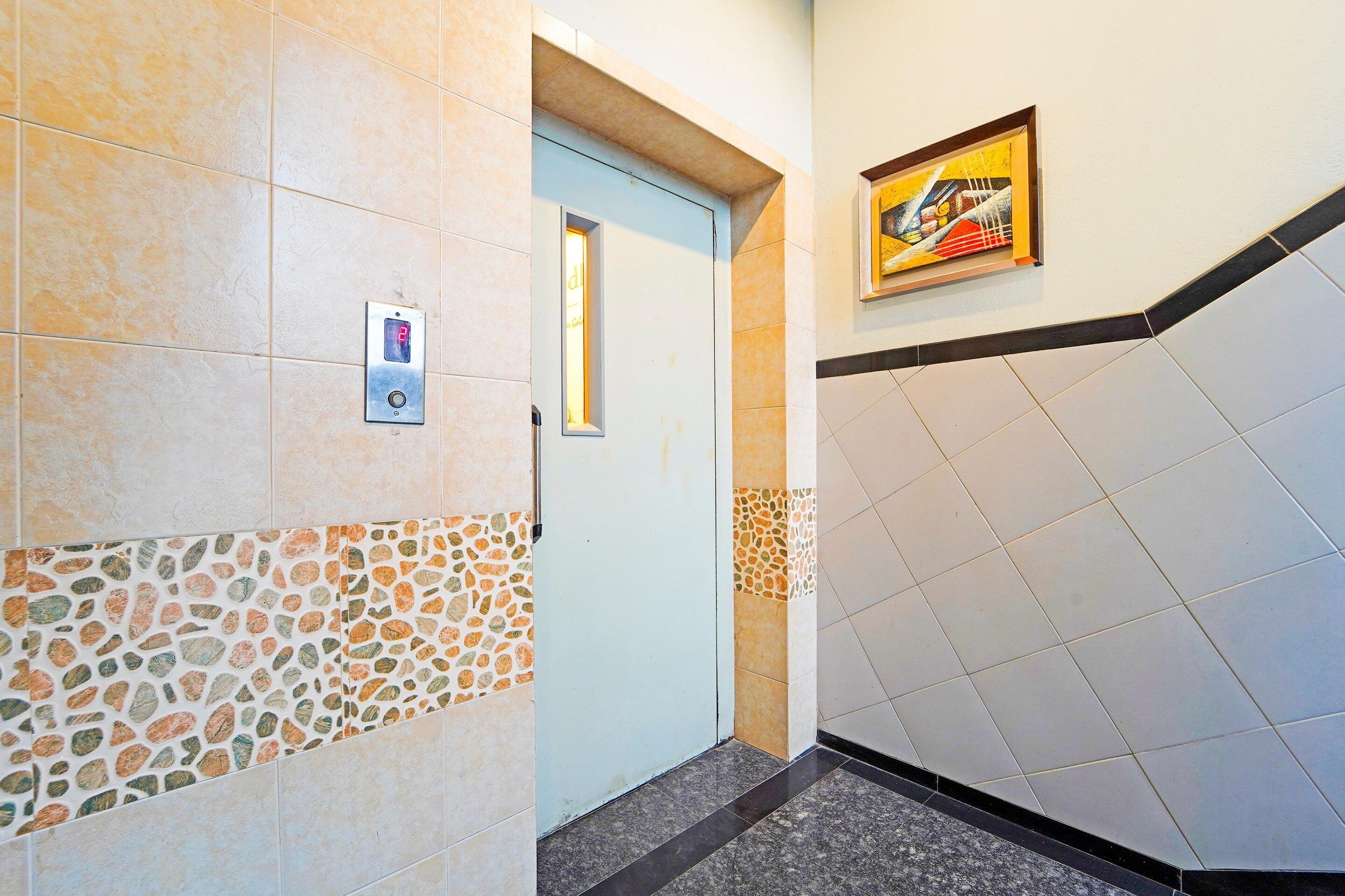 A hallway with a door, a digital elevator control panel, a framed artwork, and a patterned wall.