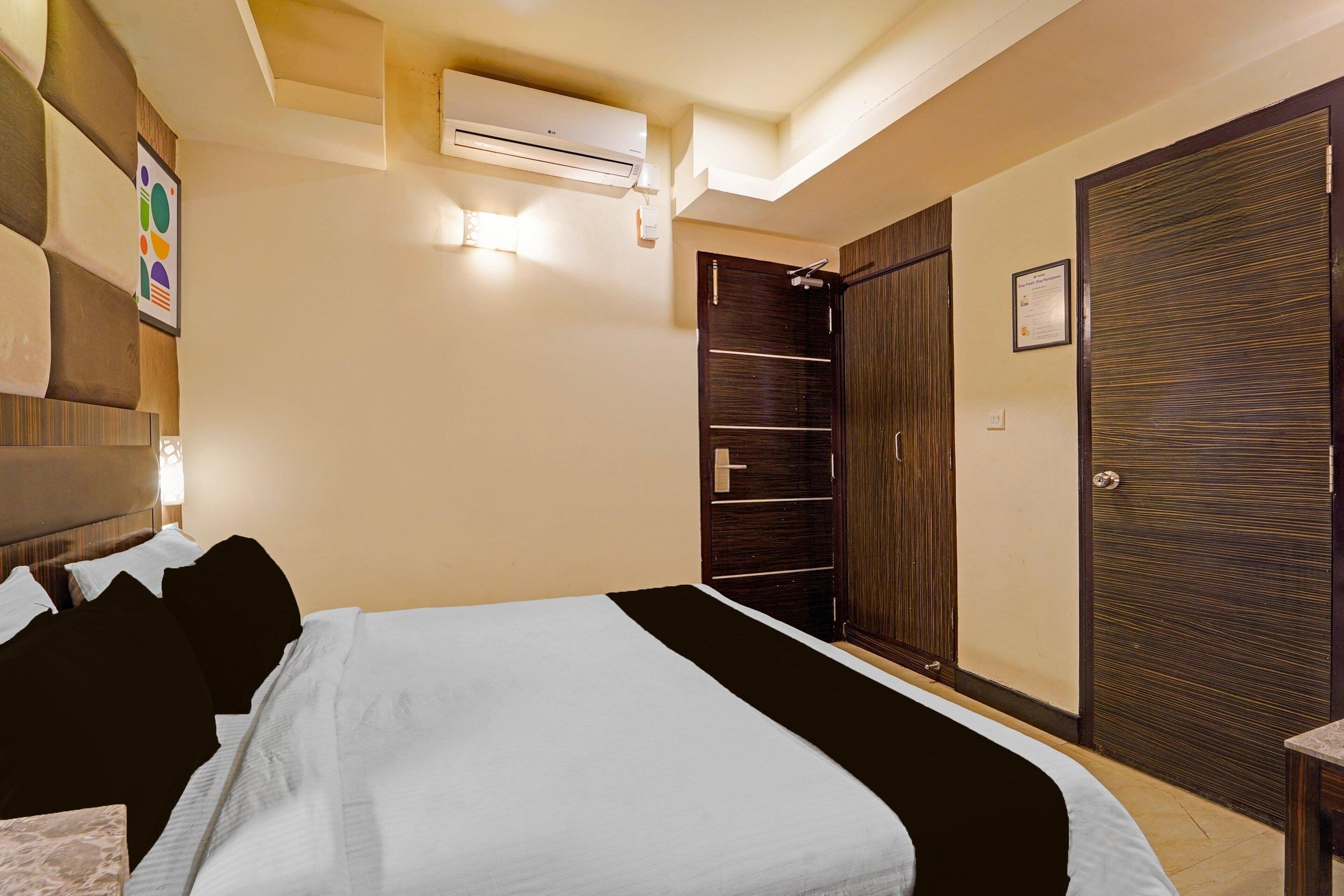 Una habitación de hotel con una cama, un armario, un equipo de aire acondicionado y una obra de arte colgada en la pared.