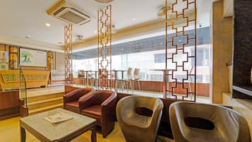 Um saguão de hotel com balcão de recepção, assentos de couro, mesa de mármore e painéis decorativos.