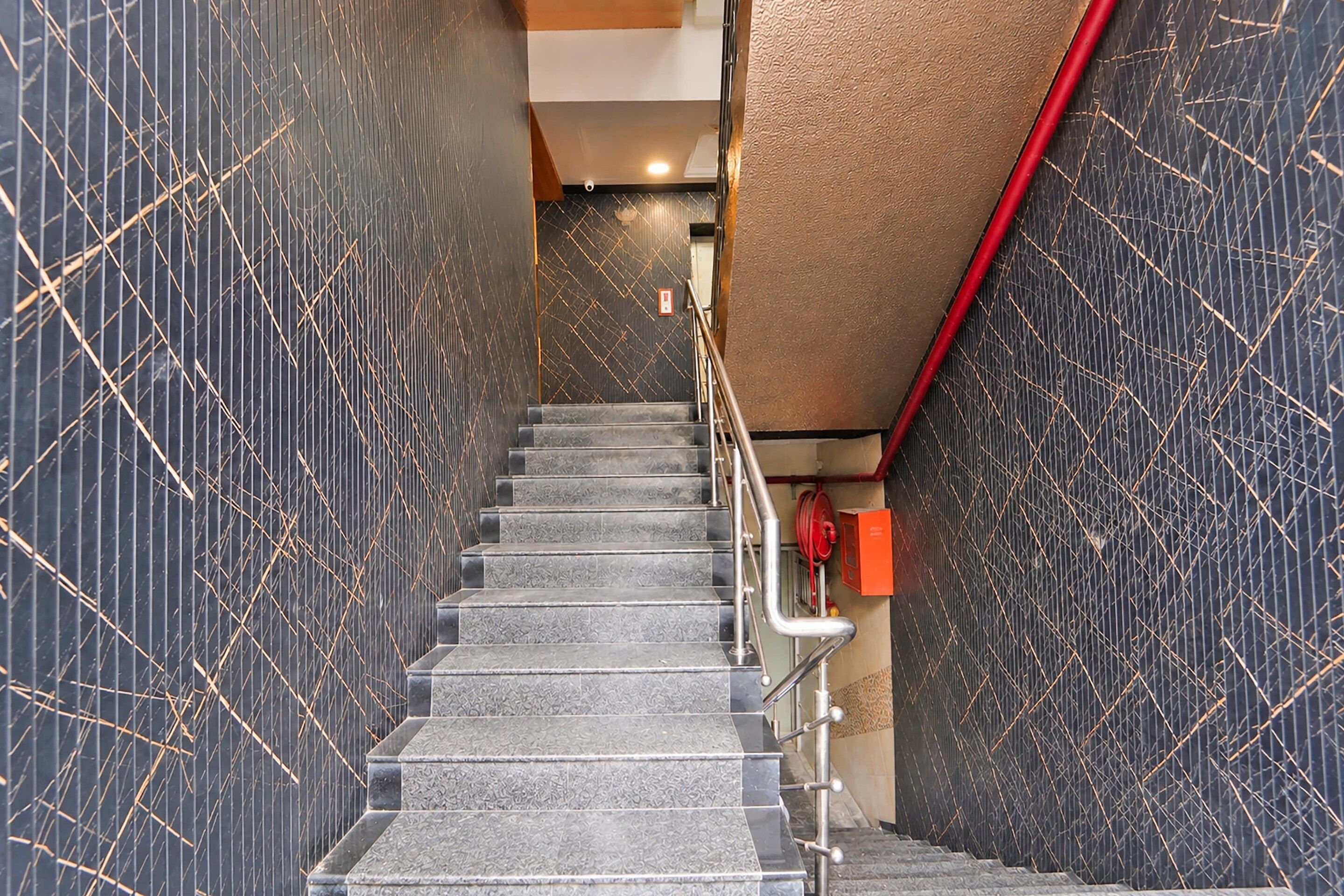 Una escalera con barandilla que conduce a un rellano con un hidrante y una tubería roja.