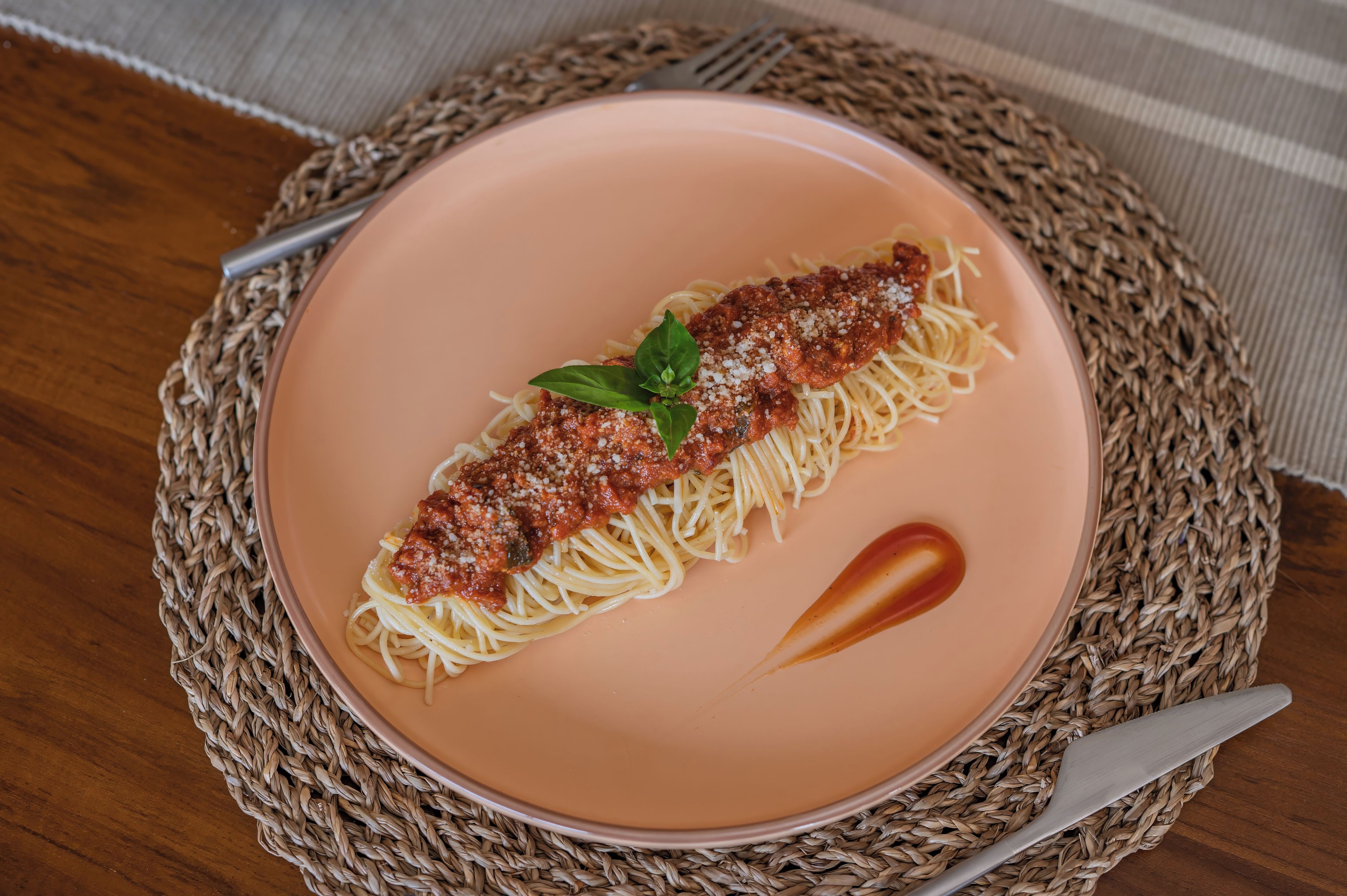 Un plato de espagueti con salsa de carne y una hoja de albahaca como decoración, sobre un camino de mesa tejido.