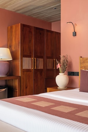 A bedroom with a bed, a wooden wardrobe, a nightstand with a lamp, and a vase with flowers.