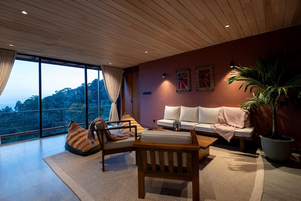 A modern living room with a large window, a sofa, a wooden coffee table, and a potted plant.