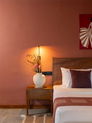 A bedroom with a wooden headboard, a bedside table with a vase of flowers, and a wall-mounted power outlet.