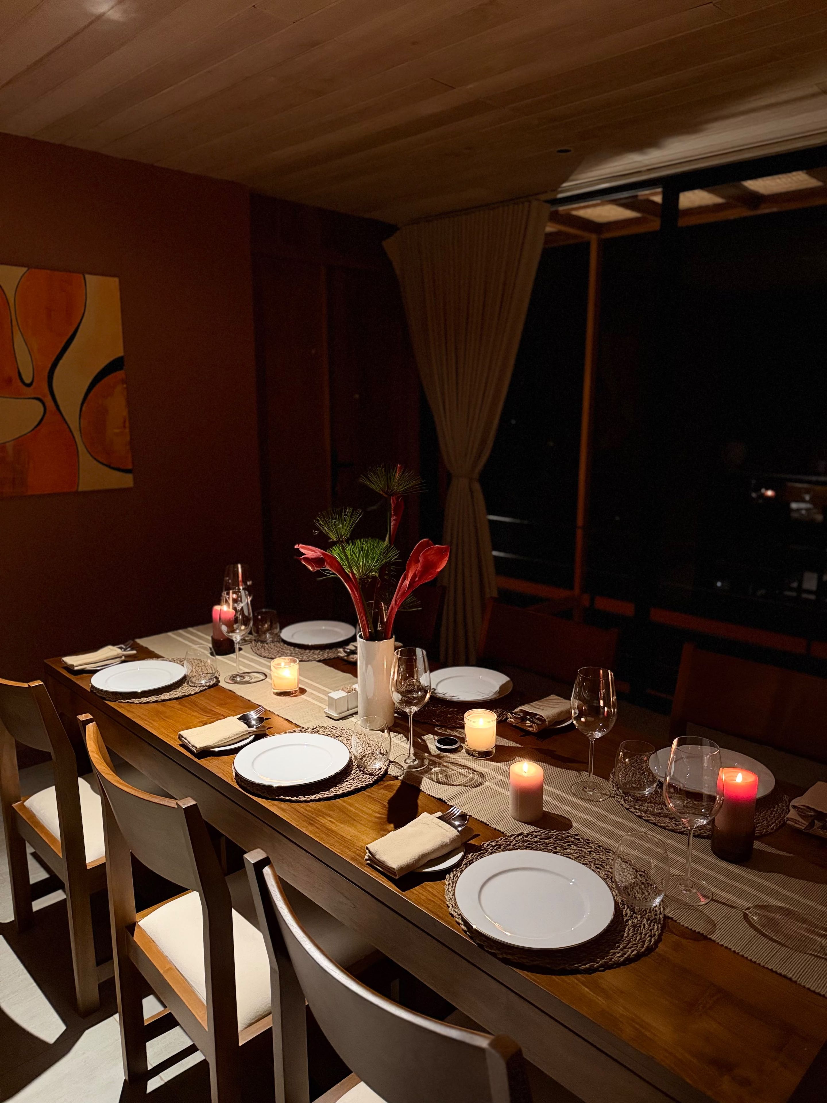A dining table set for six with candles, a vase with flowers, and a city view.