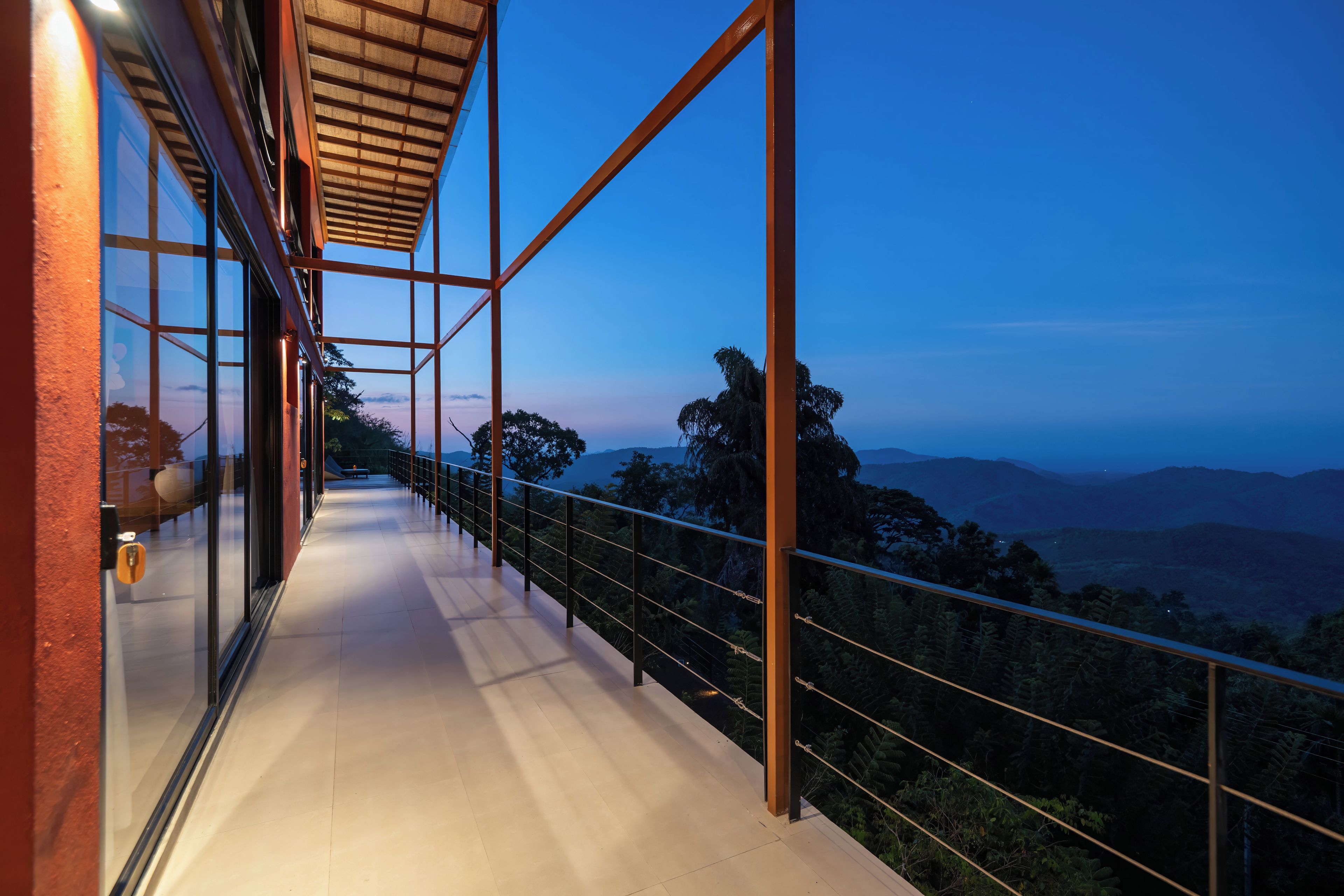 A corridor with glass walls and metal railings, leading to a scenic view of a mountainous landscape.