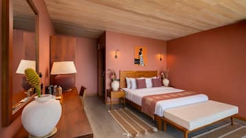 Habitación de hotel con techo de madera, cama con cabecera, mesita de noche con lámpara, un jarrón grande y una obra de arte colgada en la pared.