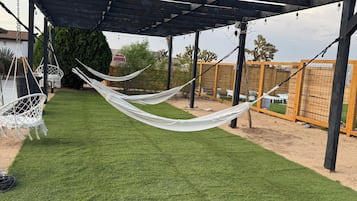 A covered outdoor area with artificial grass, a hammock, and a pergola structure.