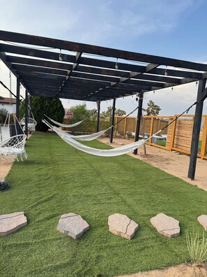 Een overdekt buitengebied met kunstgras, een hangmat en een pergola.