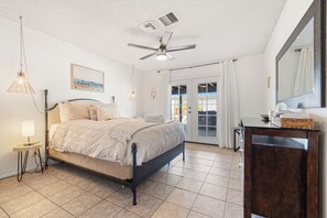 Une chambre à coucher comprenant un lit, une table de chevet, une lampe, un ventilateur de plafond et une vue sur l’extérieur grâce à une porte coulissante.