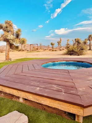 Une terrasse en bois entoure une piscine, avec une végétation désertique en arrière-plan.